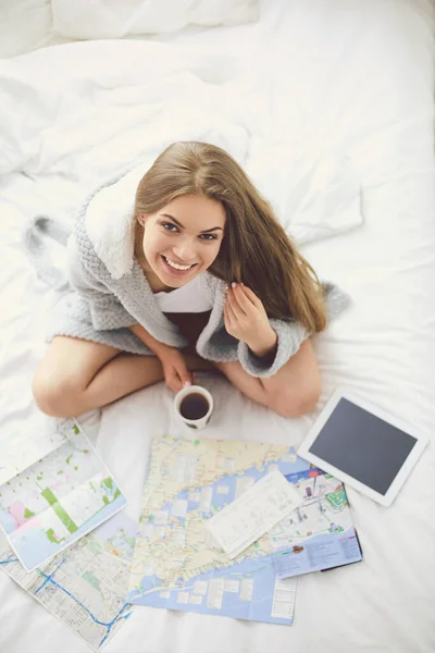 Relaxado jovem mulher sentada na cama com uma xícara de café e tablet digital — Fotografia de Stock