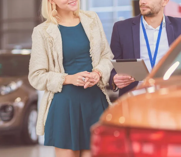 ショールームで女性とディーラーは新しい車の近くに立つ — ストック写真