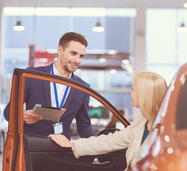 美丽的年轻女子在经销商处选择一辆车时说话帅汽车经销店工人 — 图库照片