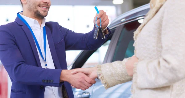 Sprzedawca samochodów sprzedaje samochód szczęśliwemu klientowi w salonie samochodowym i przekazuje klucze. — Zdjęcie stockowe