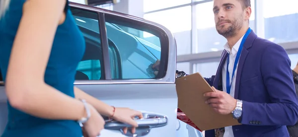 Negociante com mulher fica perto de um carro novo no showroom — Fotografia de Stock