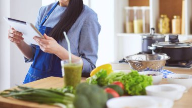 Mutfakta yemek yapmak için tablet bilgisayar kullanan genç bir kadın.