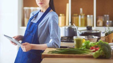 Mutfakta yemek yapmak için tablet bilgisayar kullanan genç bir kadın.