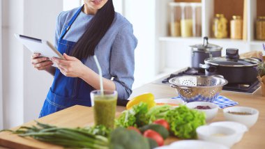 Mutfakta yemek yapmak için tablet bilgisayar kullanan genç bir kadın.