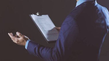 Başarılı, neşeli genç adamın portresi. Yeni ürünü sunuyor. Gri arka planda fotokopi spazmını gösteriyor.