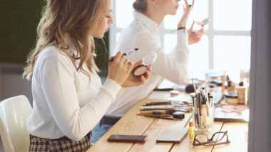 Makyaj sanatçısı, mankenlerin gözüne beyaz göz farı sürüyor ve arka planda göz farı olan bir kabuk tutuyor.