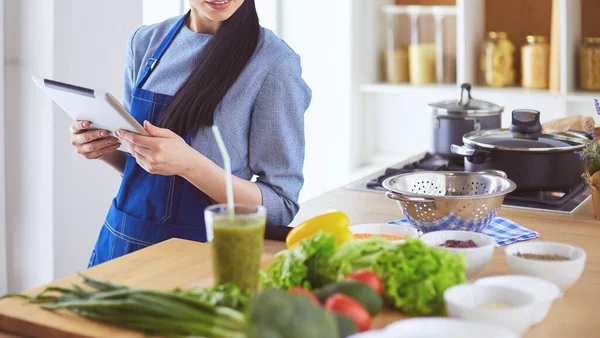 Mutfakta yemek yapmak için tablet bilgisayar kullanan genç bir kadın.