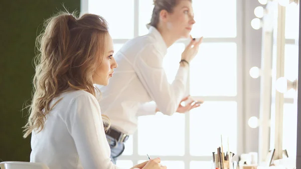 Make-up malíř nanášení bílých očních stínů v koutku oka modelů a držení skořápky s očním stínem na pozadí — Stock fotografie