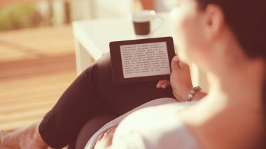 Touchpad ile kanepede oturan gülümseyen genç kadın.