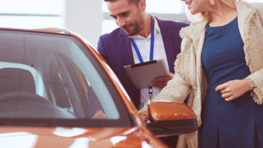 Kadın satıcısı galeride yeni bir arabanın yanında duruyor.