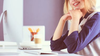 Ofis masasında çalışan ve dizüstü bilgisayarla yazan kendine güvenen genç bir iş kadını.