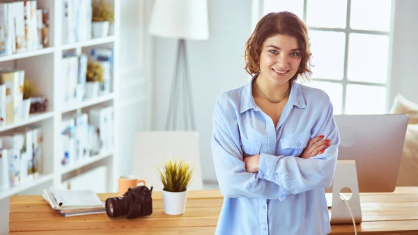 Fotógrafa sonriente con una cámara profesional de pie cerca del escritorio —  Fotos de Stock