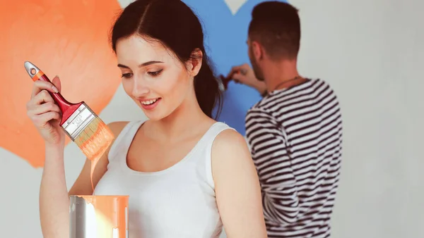 Porträtt av glada leende unga par målning interiör vägg i nytt hus. unga par — Stockfoto