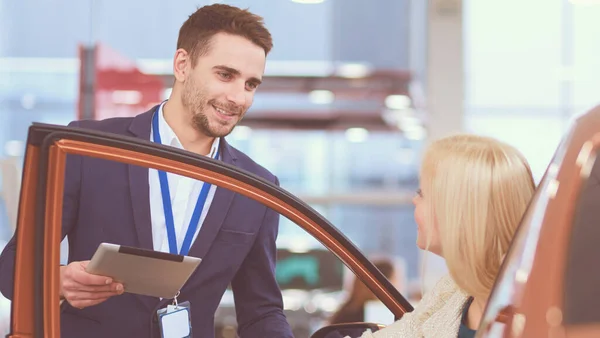 Hermosa mujer joven está hablando con el trabajador de concesionario de automóviles guapo al elegir un coche en concesionario — Foto de Stock