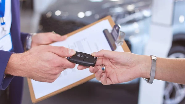 Продавец автомобилей продает автомобиль счастливому клиенту в автосалоне и передает ключи — стоковое фото
