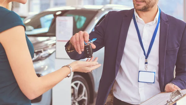 車の販売員は車の販売代理店で幸せな顧客に車を販売し、キーの上に手 — ストック写真