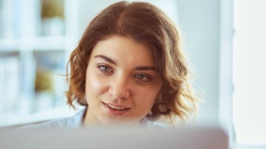 Mutlu güzel kadın rahat koltukta dizüstü bilgisayar kullanıyor.