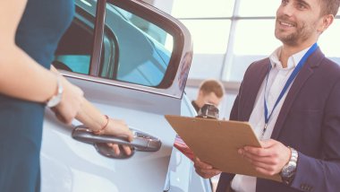 Kadın satıcısı galeride yeni bir arabanın yanında duruyor.