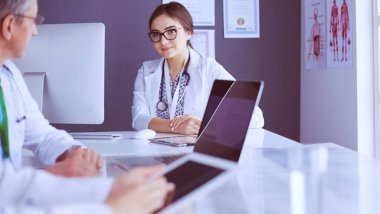 Ciddi bir tıbbi ekip parlak bir ofiste dizüstü bilgisayar kullanıyor.