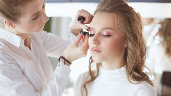 Young beautiful bride applying wedding make-up by professional make-up artist — Stock Photo, Image