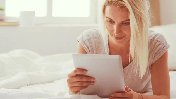 Chica sosteniendo tableta digital con pantalla en blanco y sonriendo a la cámara en el dormitorio — Foto de Stock