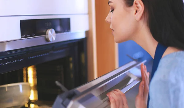 Hermosa joven comprobando cómo le va a su pastel en el horno — Foto de Stock