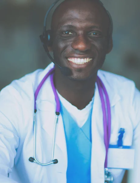 Klinikteki masada bilgisayar kullanırken kulaklık takan genç erkek doktorun portresi. — Stok fotoğraf