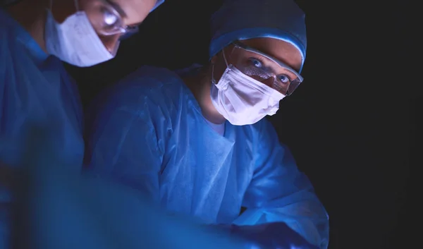 Équipe de médecins en chirurgie dans un fond sombre. — Photo