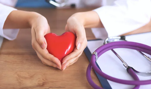 Ung läkare med röd hjärtsymbol sitter vid skrivbordet isolerad — Stockfoto