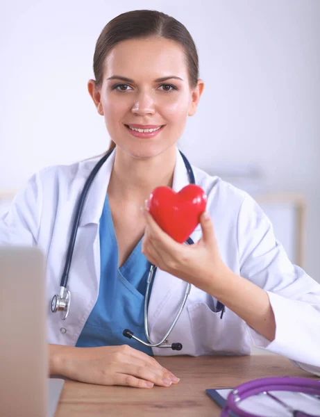Junger Arzt mit rotem Herzsymbol sitzt am Schreibtisch — Stockfoto