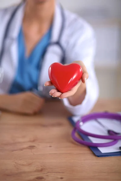 Jeune médecin avec symbole de coeur rouge assis au bureau isolé — Photo