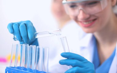 Kadın araştırmacı, beyaz arka planda izole edilmiş ilaç şişeleri ve mataralarla çevrili.