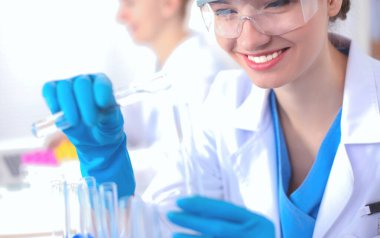 Kadın araştırmacı, beyaz arka planda izole edilmiş ilaç şişeleri ve mataralarla çevrili.