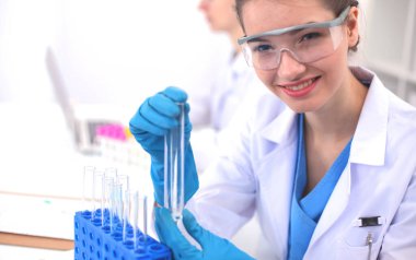 Kadın araştırmacı, beyaz arka planda izole edilmiş ilaç şişeleri ve mataralarla çevrili.