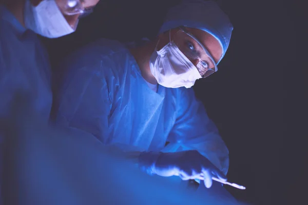 Equipe de médicos em cirurgia em um fundo escuro. — Fotografia de Stock