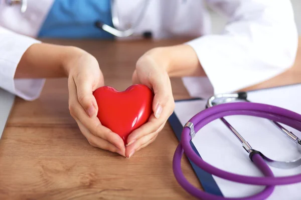 Joven médico con el símbolo del corazón rojo sentado en el escritorio aislado — Foto de Stock