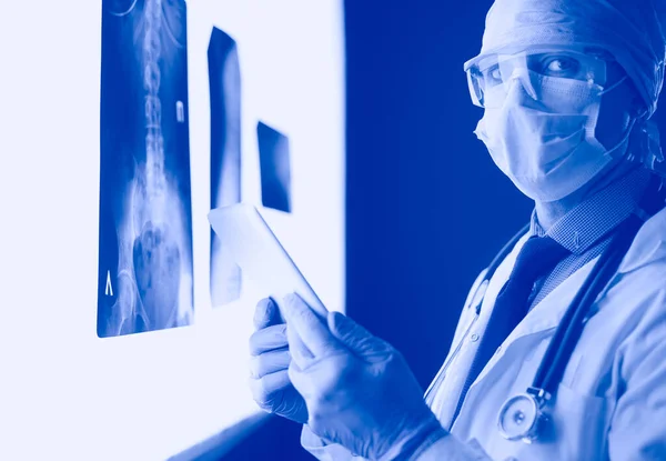 Doctor in hospital sitting at desk looking at x-rays on tablet against white background with x-rays — Stock Photo, Image