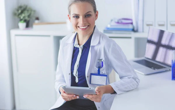 Portrét doktorky na chodbě nemocnice, držící počítač, dívající se do kamery, usmívající se — Stock fotografie