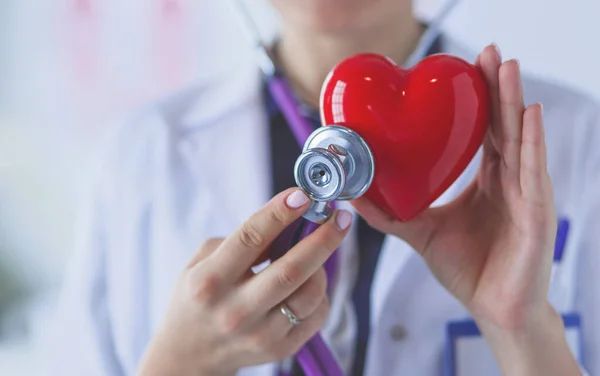 Un médecin avec stéthoscope examinant le cœur rouge, isolé sur fond blanc — Photo