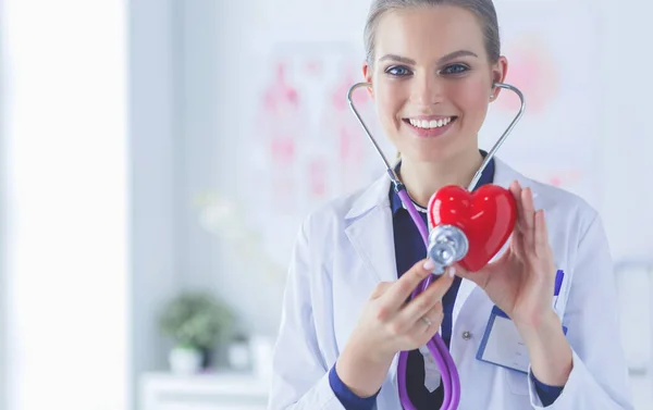 Lékař se stetoskopem vyšetřuje červené srdce, izolované na bílém pozadí — Stock fotografie