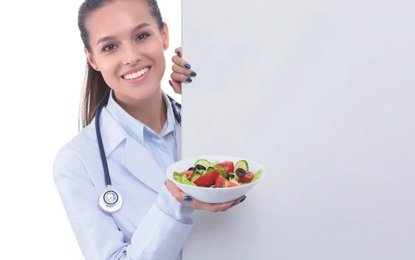 Retrato de uma mulher bonita médico segurando um prato com legumes frescos em pé perto de branco. Mulheres médicas — Fotografia de Stock