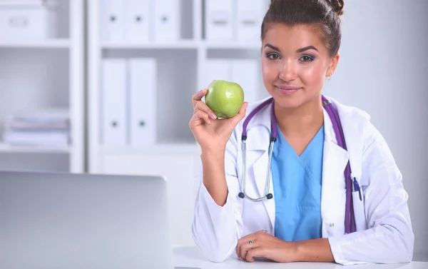 Female doctor hand holding a green apple, sitting at the desk — Stock Photo, Image