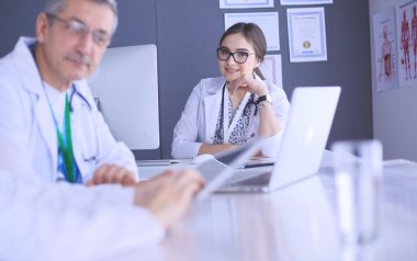 Ciddi bir tıbbi ekip parlak bir ofiste dizüstü bilgisayar kullanıyor.