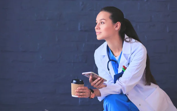 Vrouwelijke arts zit met mobiele telefoon en het drinken van koffie — Stockfoto