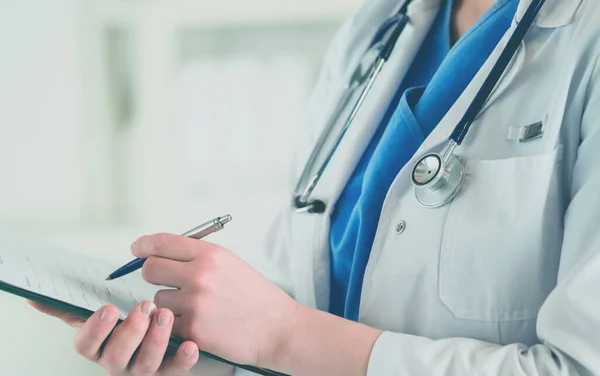 청진기를 들고, 손에 공책을 들고 있는 의사. 병원에서 똑바로 서 있는 한 여의사가 클립보드에서 의학적 서류를 작성하는 모습 — 스톡 사진