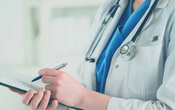 Doctor con un estetoscopio, sosteniendo un cuaderno en su mano. Primer plano de una doctora llenando el formulario médico en el portapapeles mientras está de pie en el hospital —  Fotos de Stock