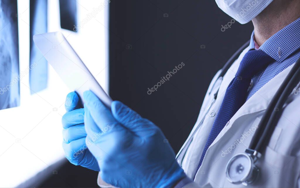 Doctor in hospital sitting at desk looking at x-rays on tablet against white background with x-rays
