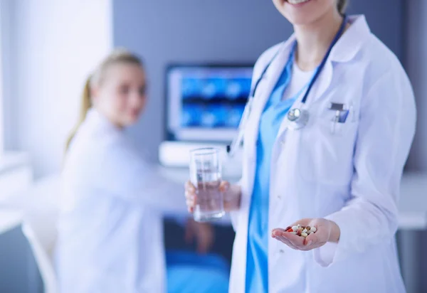 Doktorun arka planda meslektaşıyla klinikte elinde haplar ve bir bardak su tutarken görüntüsü.. — Stok fotoğraf