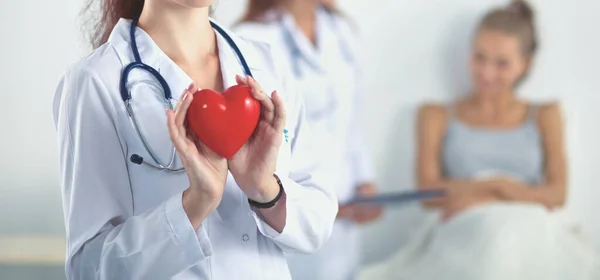 Young woman doctor holding a red heart, standing on gray background — Stock Photo, Image