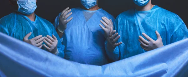 Grupo de cirurgiões no trabalho em sala de operações tonificada em azul. Equipe médica realizando operação — Fotografia de Stock